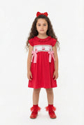 Young girl wearing a red dress with white smocking  and embroidered cherry details on a white background
