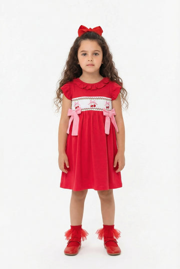 Young girl wearing a red dress with white smocking  and embroidered cherry details on a white background