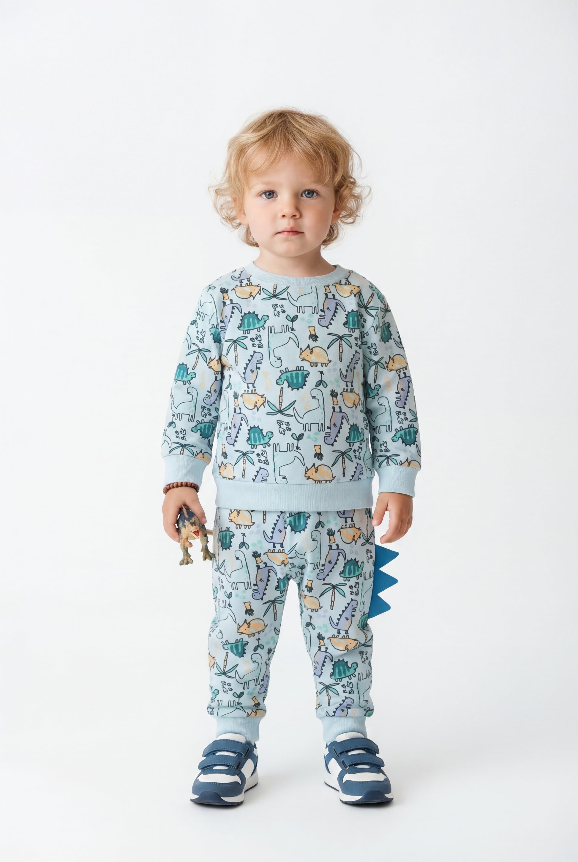 Child wearing a patterned dinosaufr jogging set with a white background
