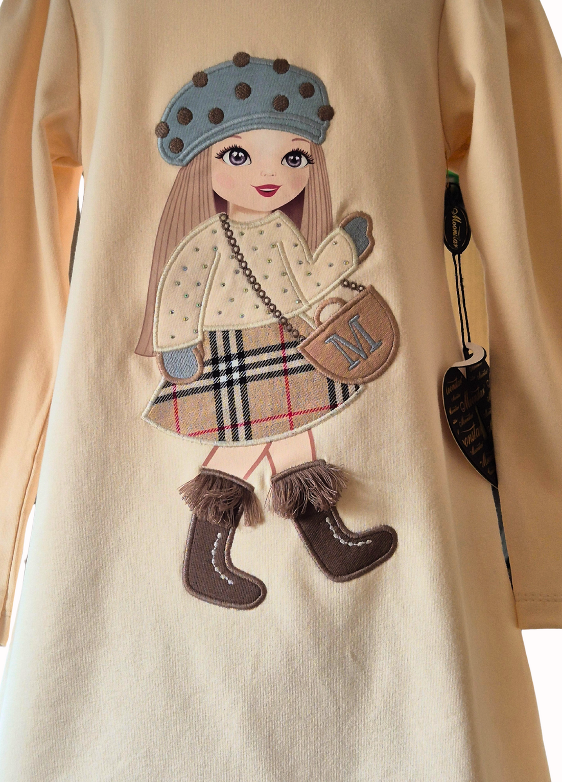 Cream dress with a large doll motif in the centre with hat, sparkle top, checked skirt and fringed boots on a white background.