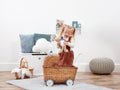Child playing with a Peter Rabbit soft toy in a wicker pram in a room with toys and cushions.