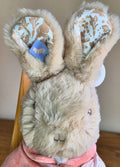 Stuffed Flopsy Rabbit with decorative ears held by a hand on a wooden surface.