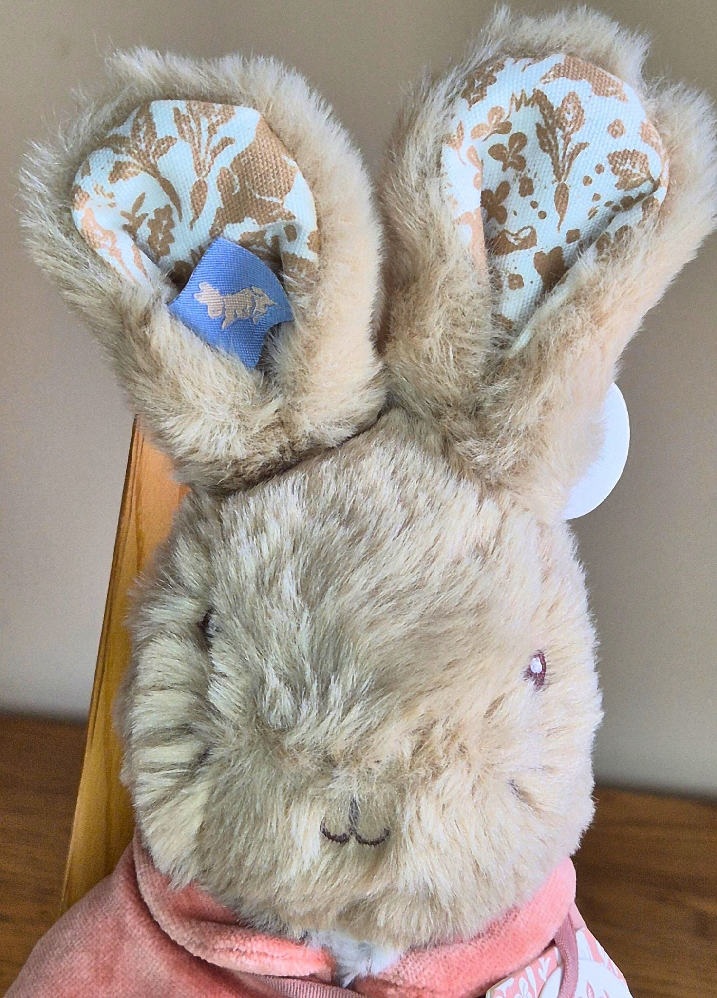 Stuffed Flopsy Rabbit with decorative ears held by a hand on a wooden surface.