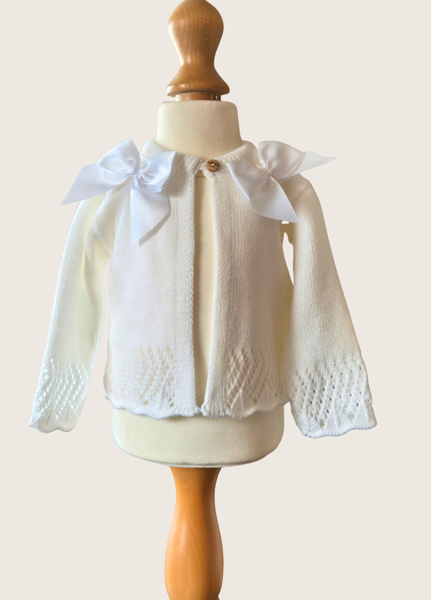 Ivory knitted cardigan with double satin bows on a mannequin against a plain background