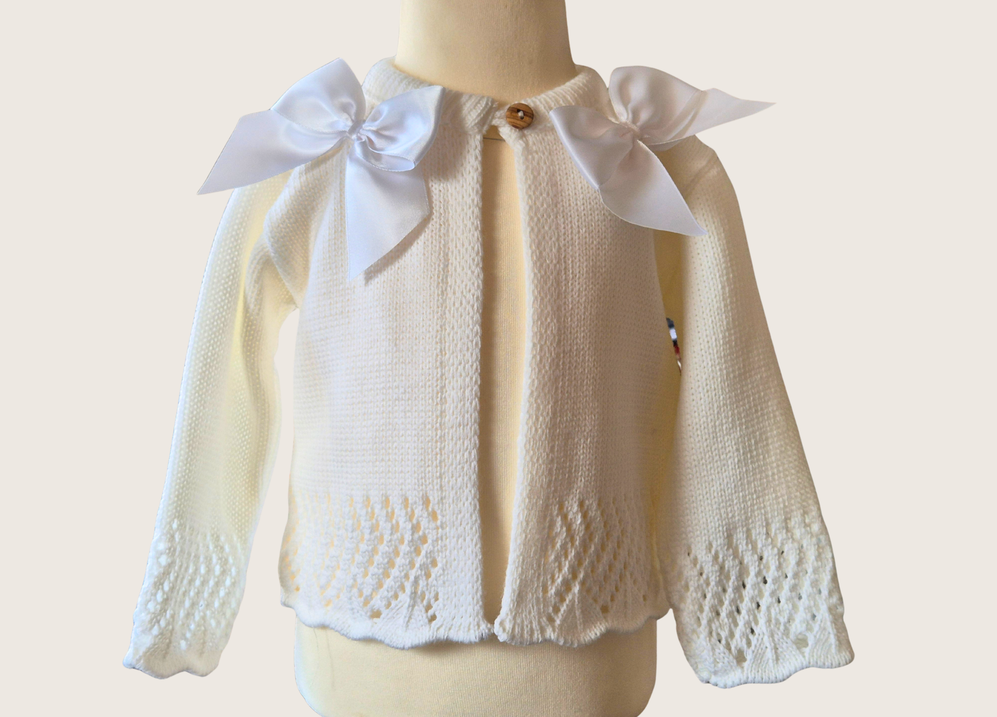 Ivory knitted cardigan with double satin bow details on a mannequin against a plain background