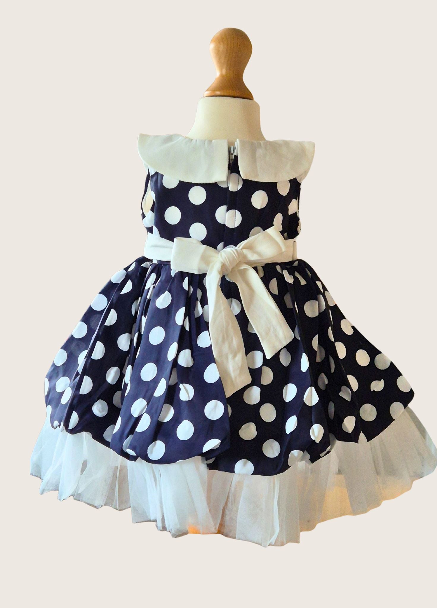 Navy blue dress with white polka dots and a large bow on a mannequin against a light background