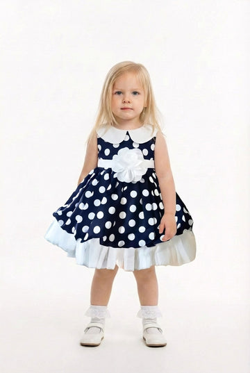 Young girl wearing a navy blue dress with white polka dots and a white collar on a white background