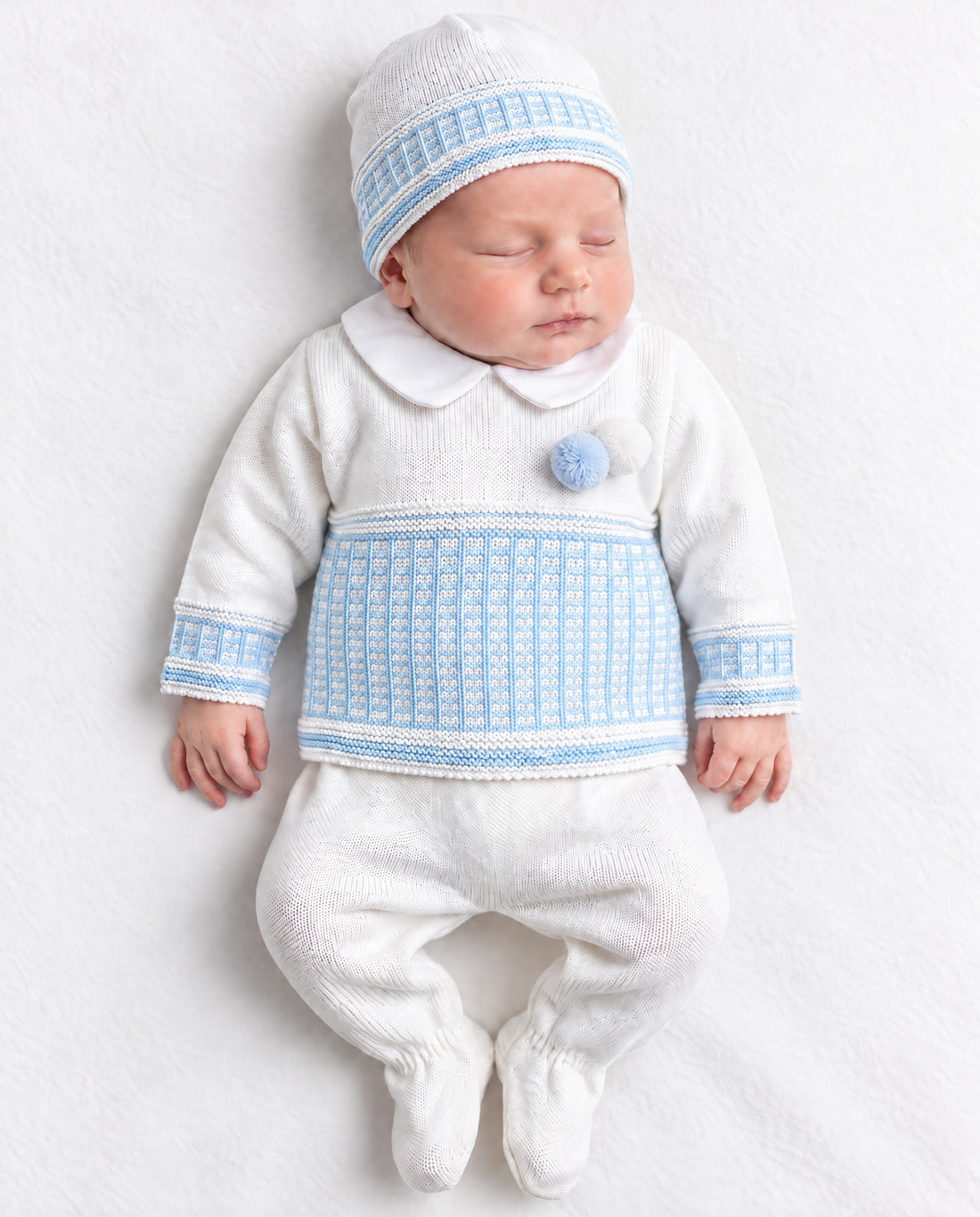 Newborn baby boys’ white and blue knitted pom pom three-piece set by Fruit De Ma Passion