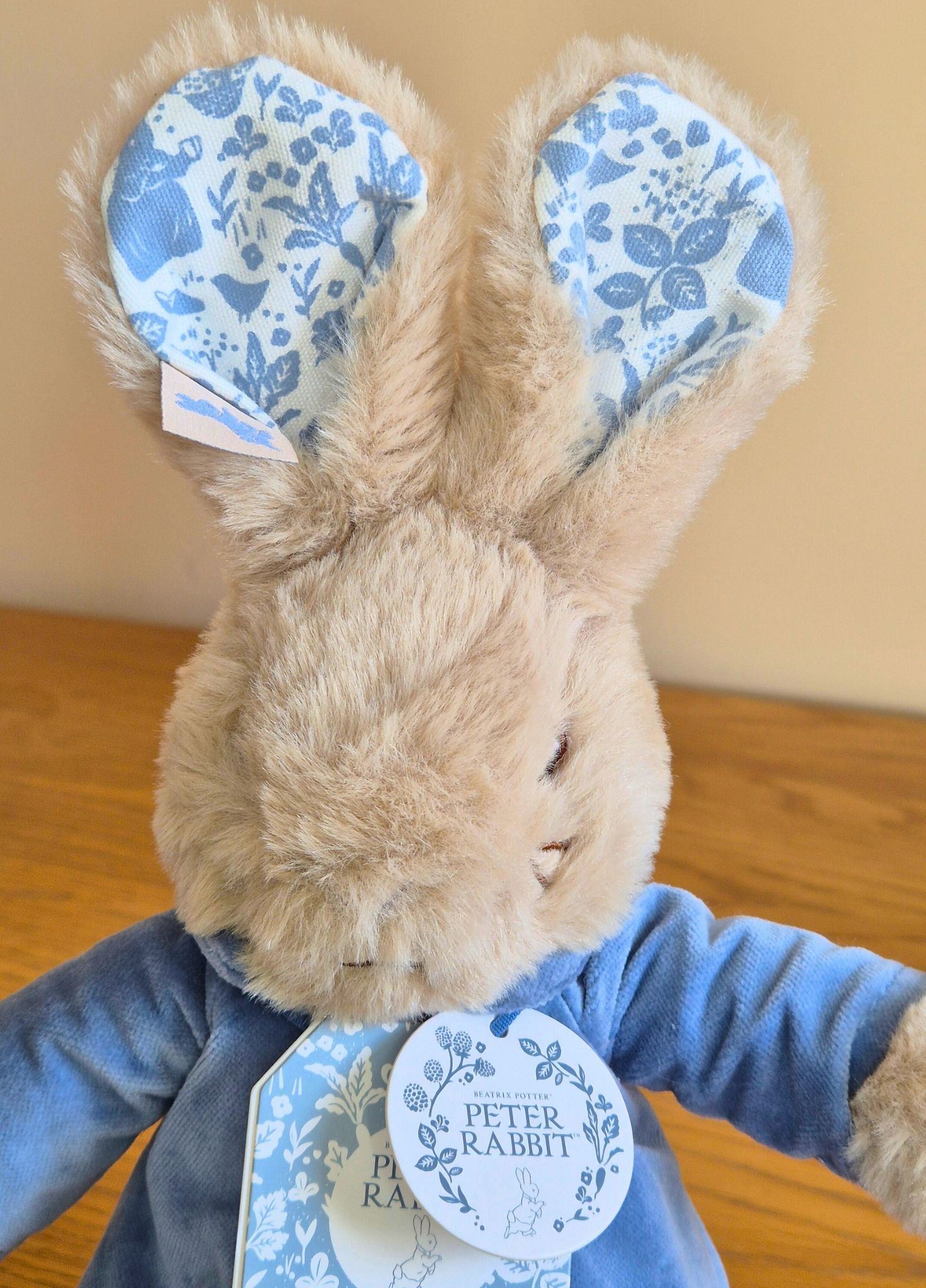 Plush toy Peter Rabbit with floral ears and a blue outfit on a wooden surface.