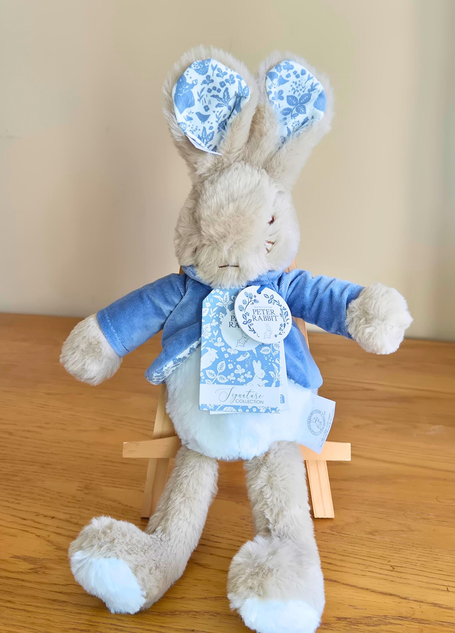 Stuffed Peter Rabbit Licensed toy with blue floral ears and outfit on a wooden surface