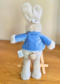 Back of Peter rabbit toy wearing a blue coat on a wooden surface with a plain background