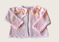 Pink knitted baby cardigan with bow details on a light pink background