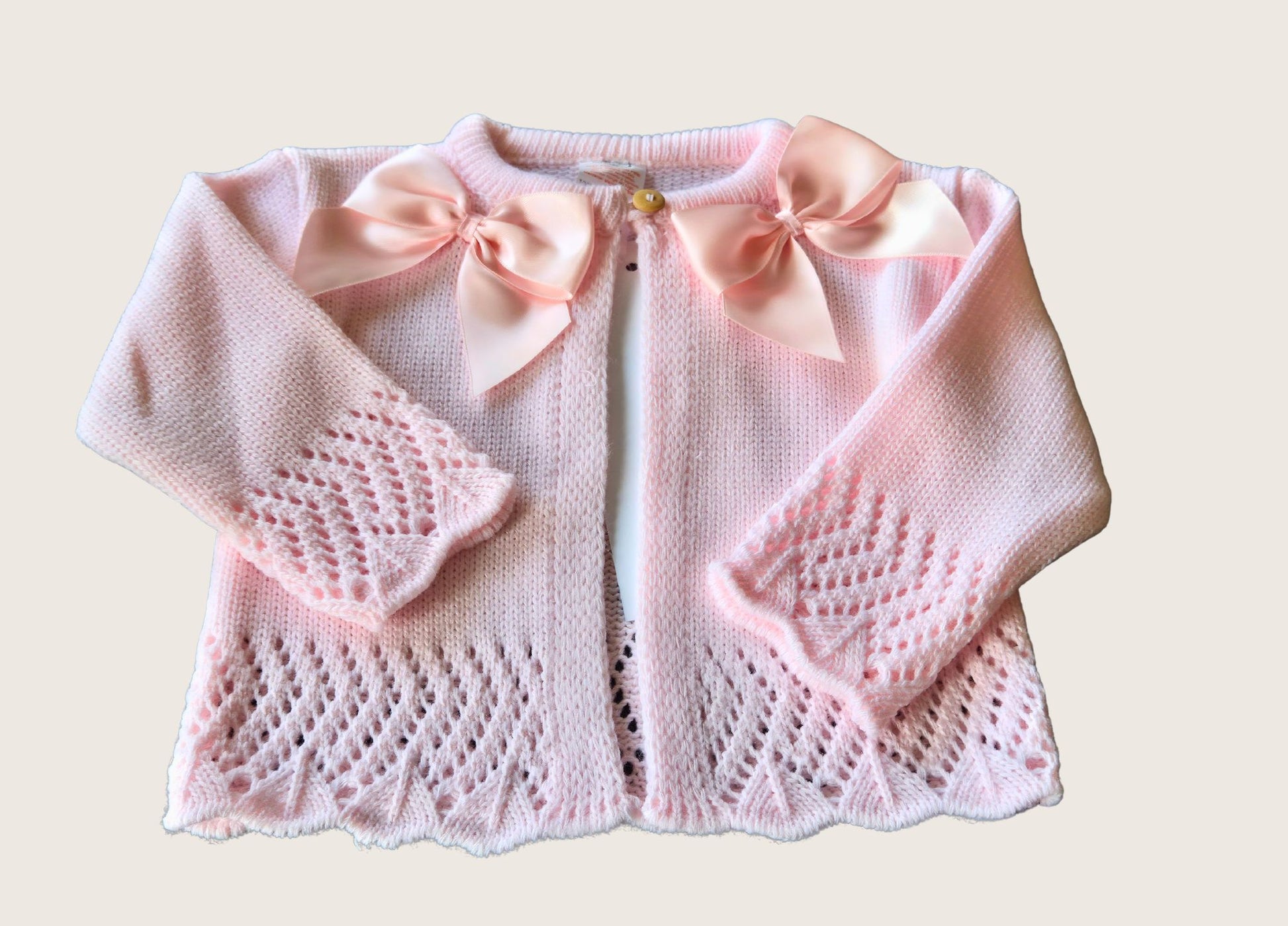 Pink knitted baby cardigan with bow details on a light pink background