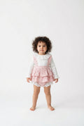 Child wearing a pink ruffled dress over a white long-sleeve shirt on a white background