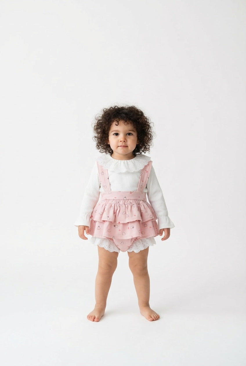 Child wearing a pink ruffled dress over a white long-sleeve shirt on a white background