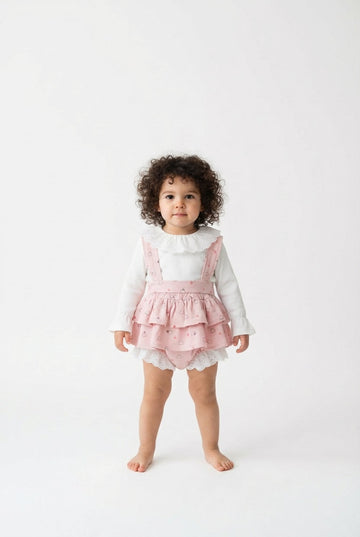 Child wearing a pink ruffled dress over a white long-sleeve shirt on a white background