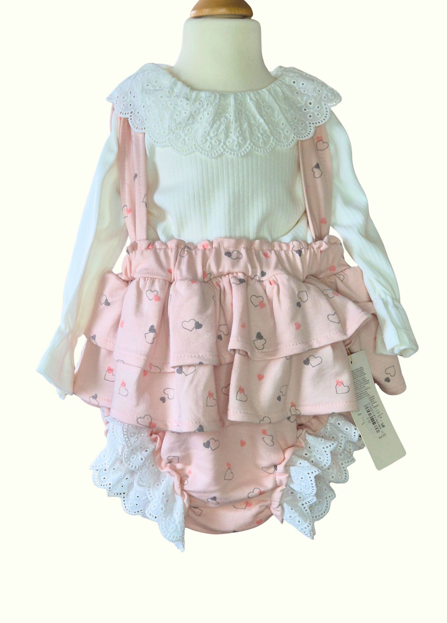 Children's outfit with pink ruffled romper and white top on a mannequin.