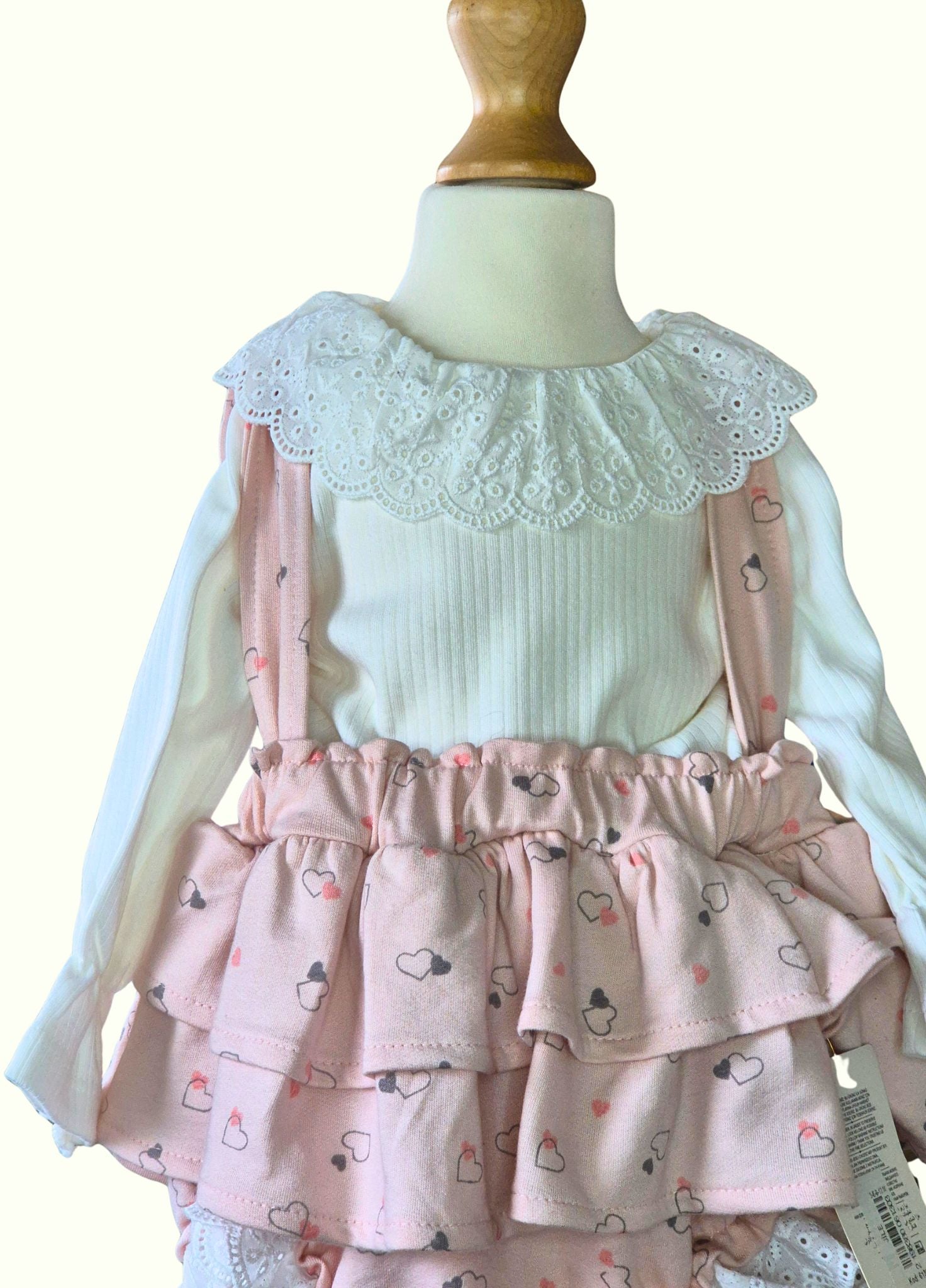 Children's outfit with a white top and pink ruffled skirted romper  on a mannequin.