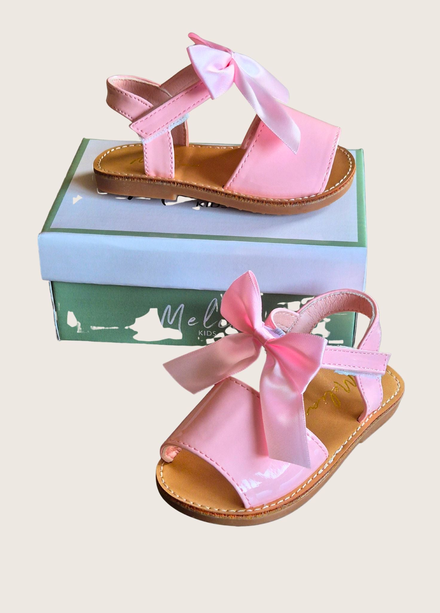 Pink children's sandals with a bow on a beige background