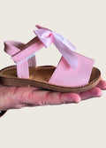 Pink sandal with a bow held in a hand against a neutral background