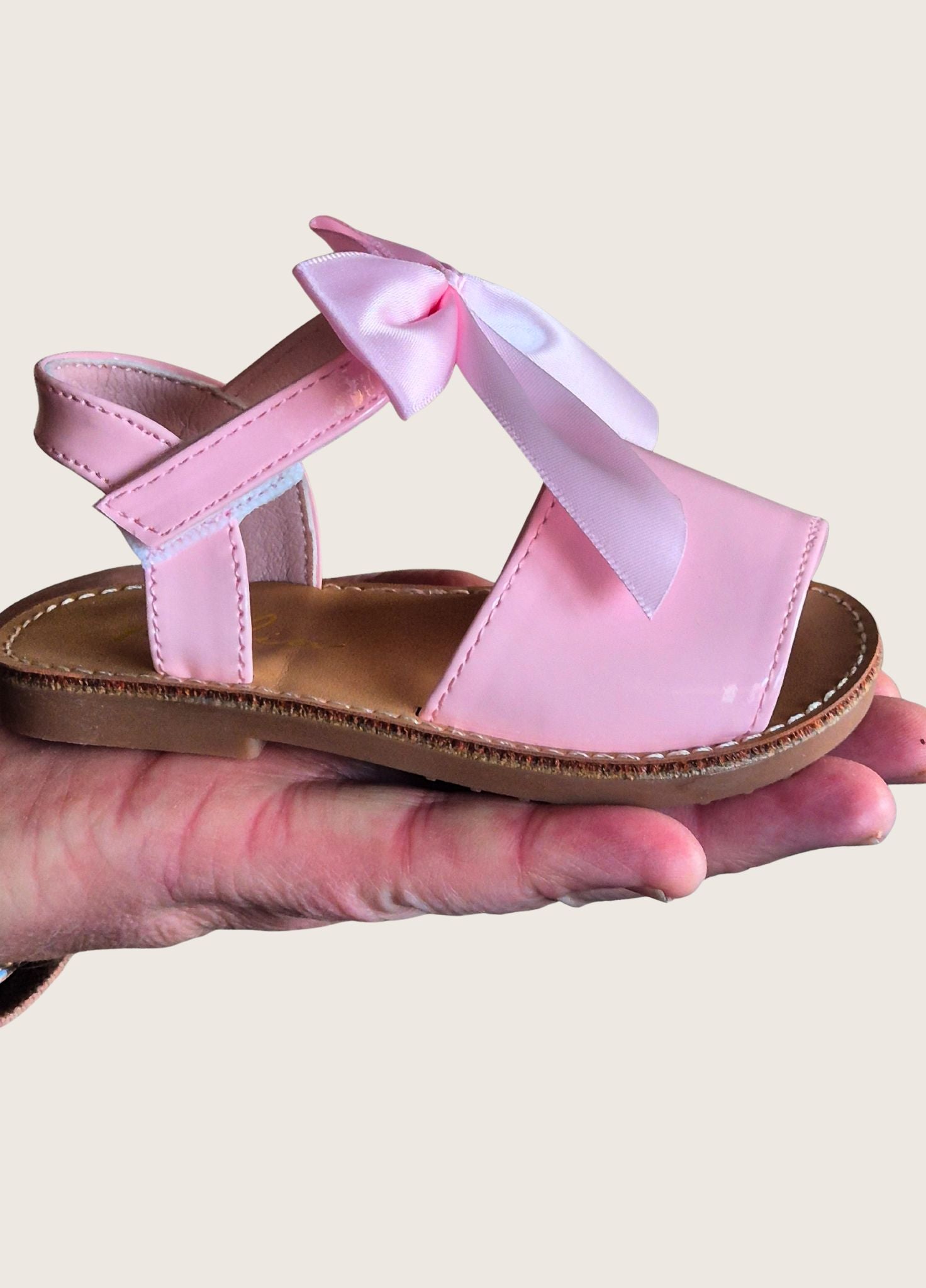 Pink sandal with a bow held in a hand against a neutral background