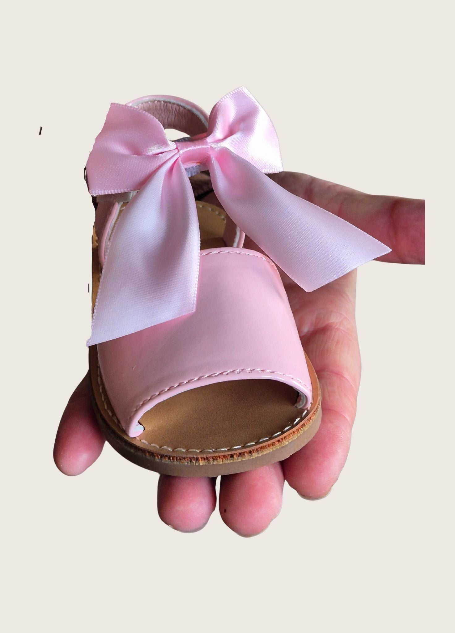 Pink sandal with a large bow held in a hand against a beige background