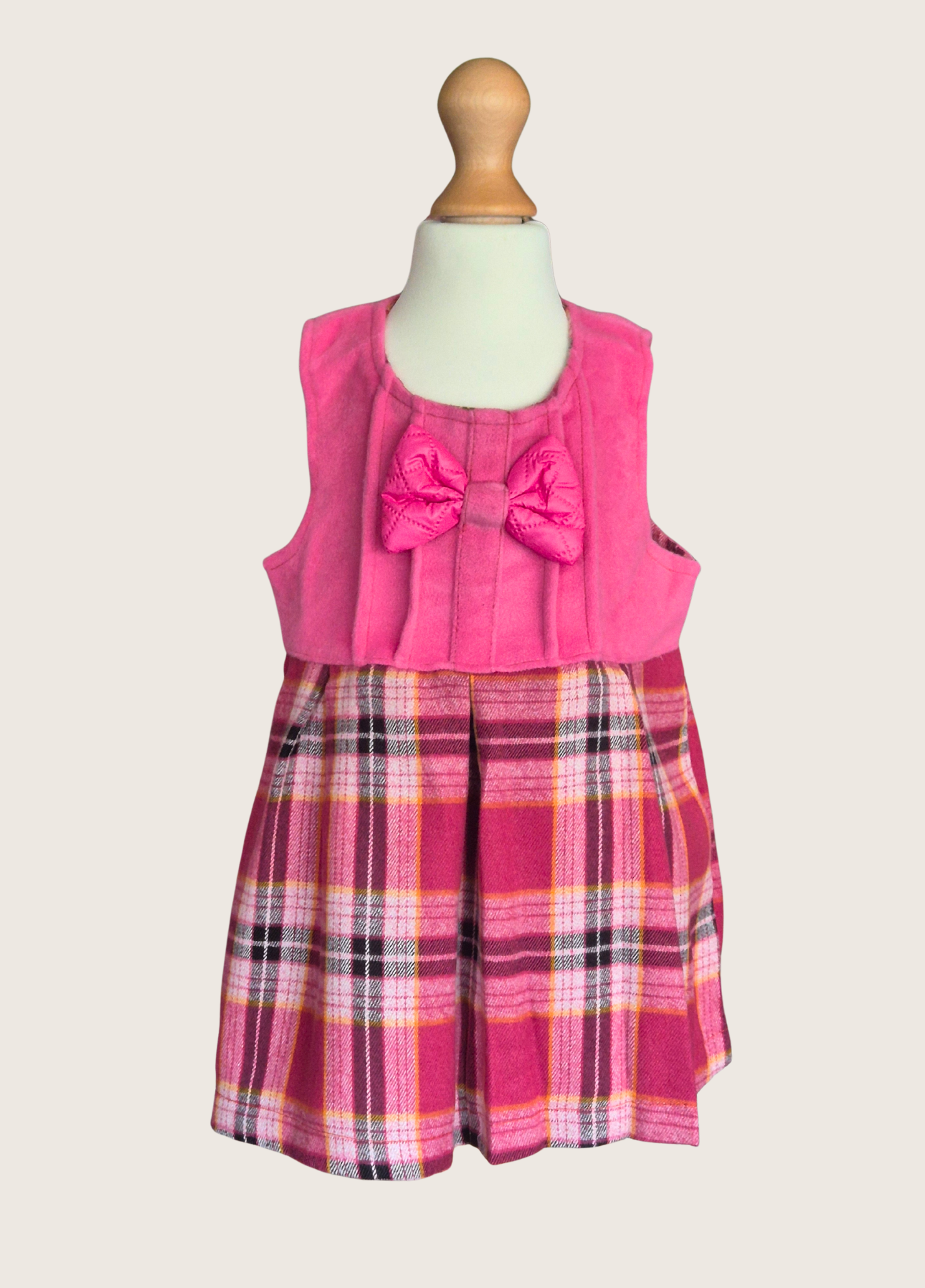 Pink plaid dress with a large bow on a mannequin against a white background