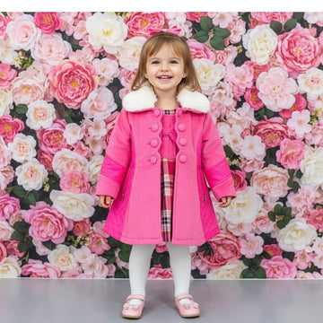 Child wearing a pink coat with white fur trim in front of a floral wall.