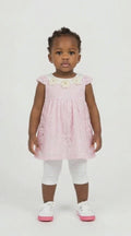 Black toddler girl in a pink lace swing dress with flower detail at the neck and white leggings on a light background.
