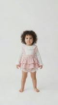 Toddler with a pink tiered frilled romper and a cream long sleeved top with a frilled collar.