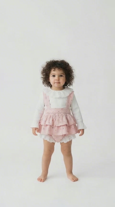 Toddler with a pink tiered frilled romper and a cream long sleeved top with a frilled collar.