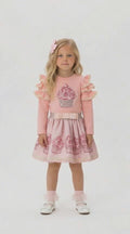 Young girl with long blonde hair in a pink co ordinating skirt and top set that features a sparkly cupcake design.