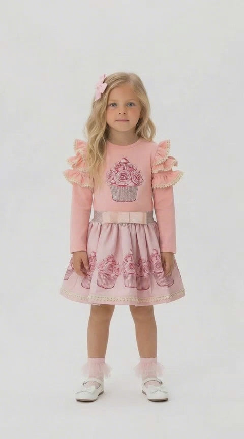 Young girl with long blonde hair in a pink co ordinating skirt and top set that features a sparkly cupcake design.