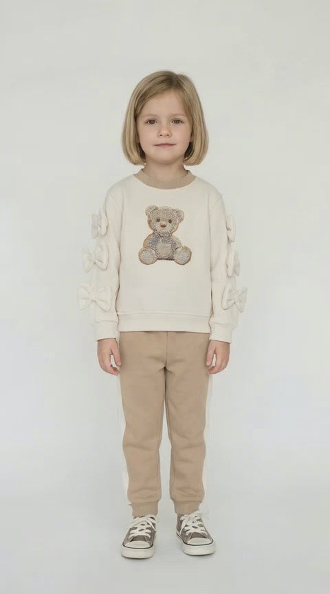 Blonde haired girl wearing a beige and cream leisure suit with a sequin encrusted teddy in the middle of the top.