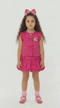 Young girl in a cerise frilled top with tie detail and matching bubble skirt on a light background.
