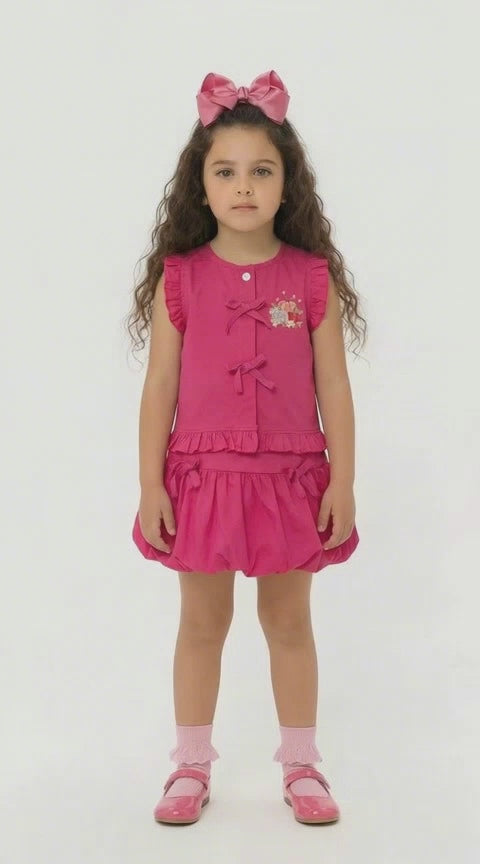 Young girl in a cerise frilled top with tie detail and matching bubble skirt on a light background.