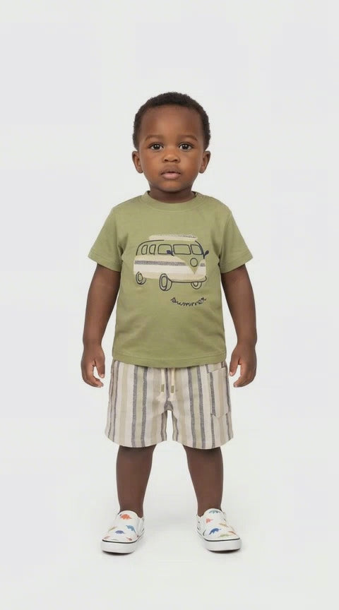 black boy toddler in an olive green t shirt with a campervan motif and a pair of cream, olive and grey striped shorts on a pale background.