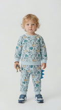 Toddler in a green multi dinosaur jogging suit with scales down one leg.  Holding a dinosaur in his hand.