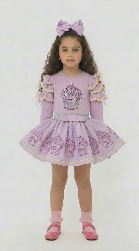 Young girl in a lilac frilled top with a sparkly cupcake design and a co ordinating lilac skirt that has cupcakes around the hemline.