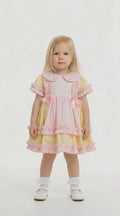 blonde hair toddler in a lemon and pink frilled dress on a white background
