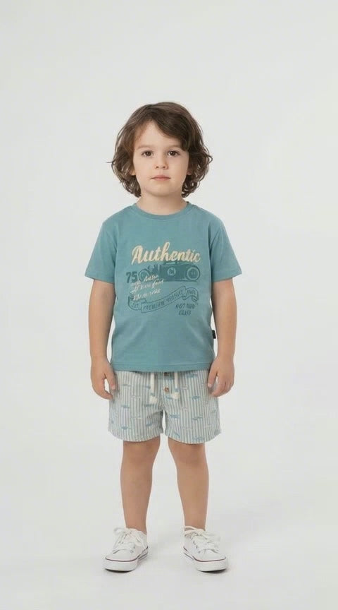 young boy in a petrol blue authentic t shirt with a classic car design and a pair of blue and cream striped linen shorts on a light background.