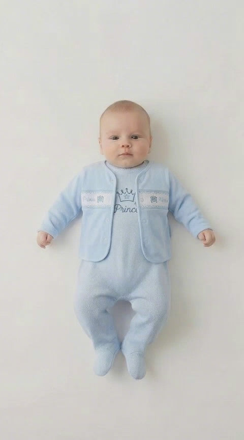 baby boy in a blue romper with a crown motif and a blue and white smocked jacket that says Prince across it