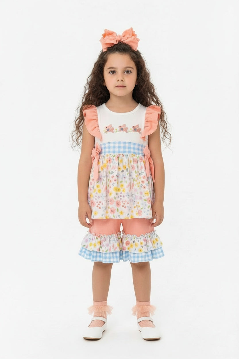 Young girl wearing a colorful floral top with ruffled sleeves and pedal pusher bottoms on a white background