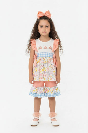 Young girl wearing a colorful floral top with ruffled sleeves and pedal pusher bottoms on a white background