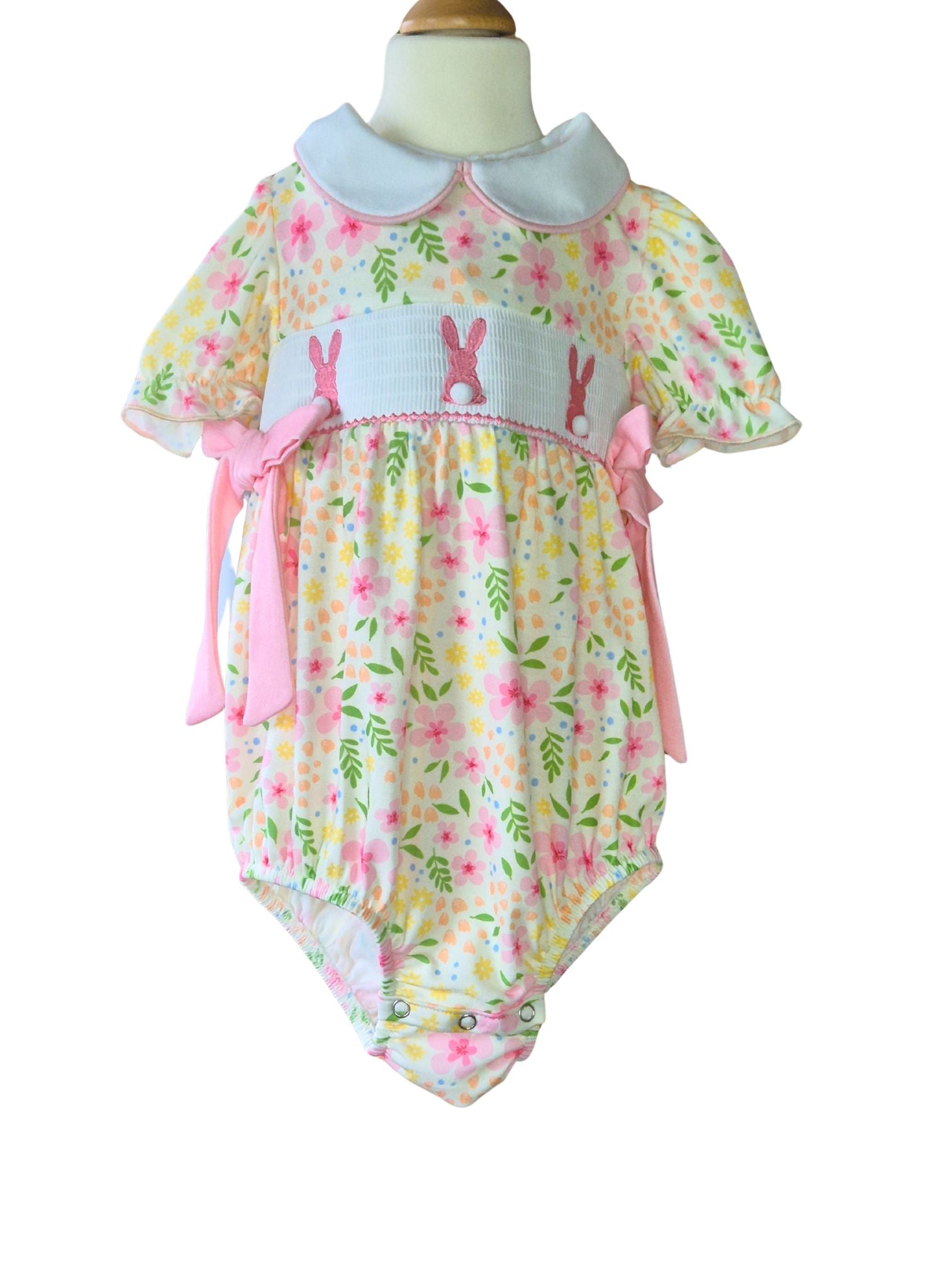 Baby romper with floral pattern and pink accents on a mannequin against a white background