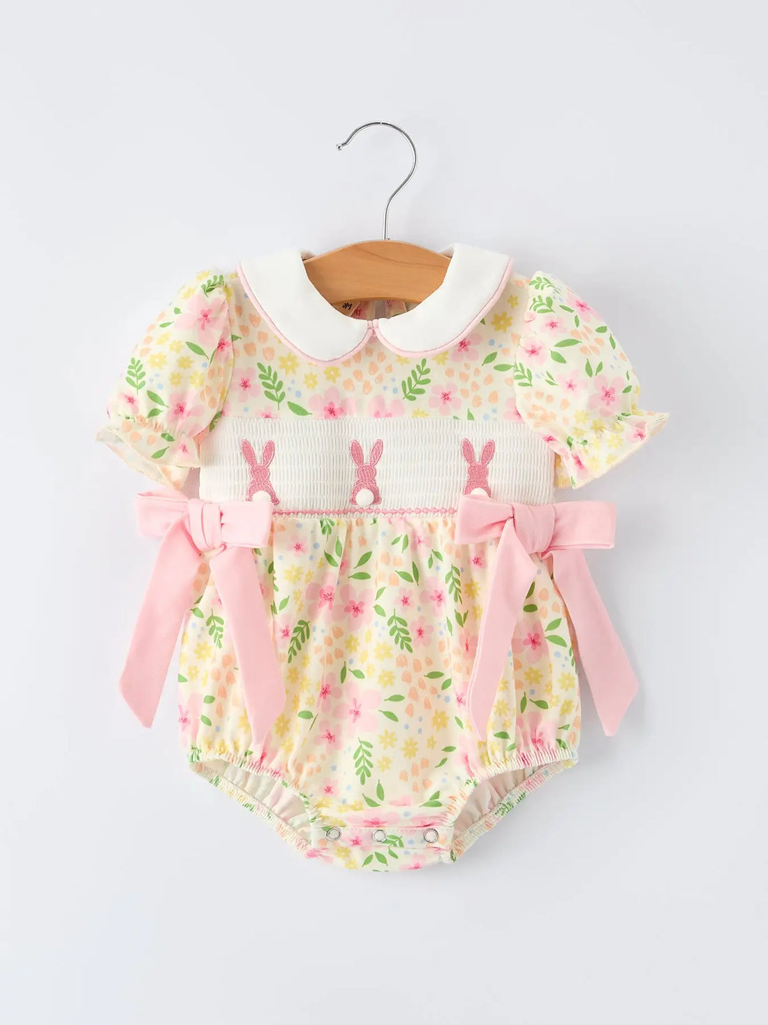 baby in a lemon floral romper with smocked rabbits on the chest and a white peter pan collar edged in pale pink on a light background.