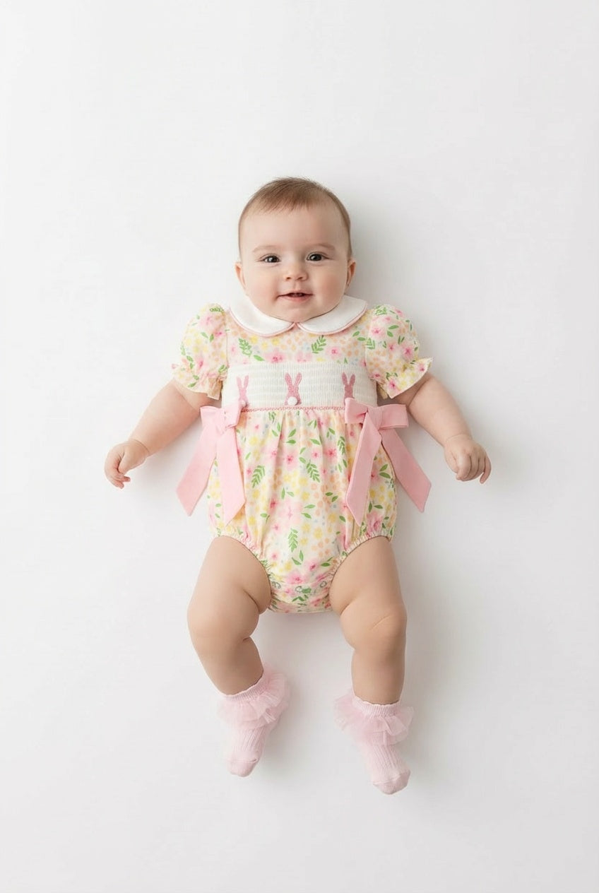Baby wearing a floral romper with pink bows on a white background