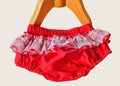 Red baby bloomers with white lace trim on a mannequin against a beige background