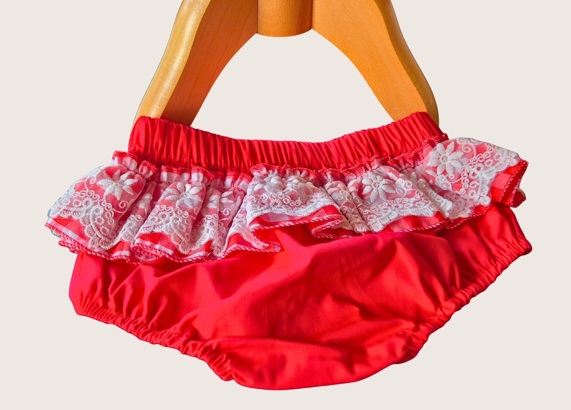 Red baby bloomers with white lace trim on a mannequin against a beige background