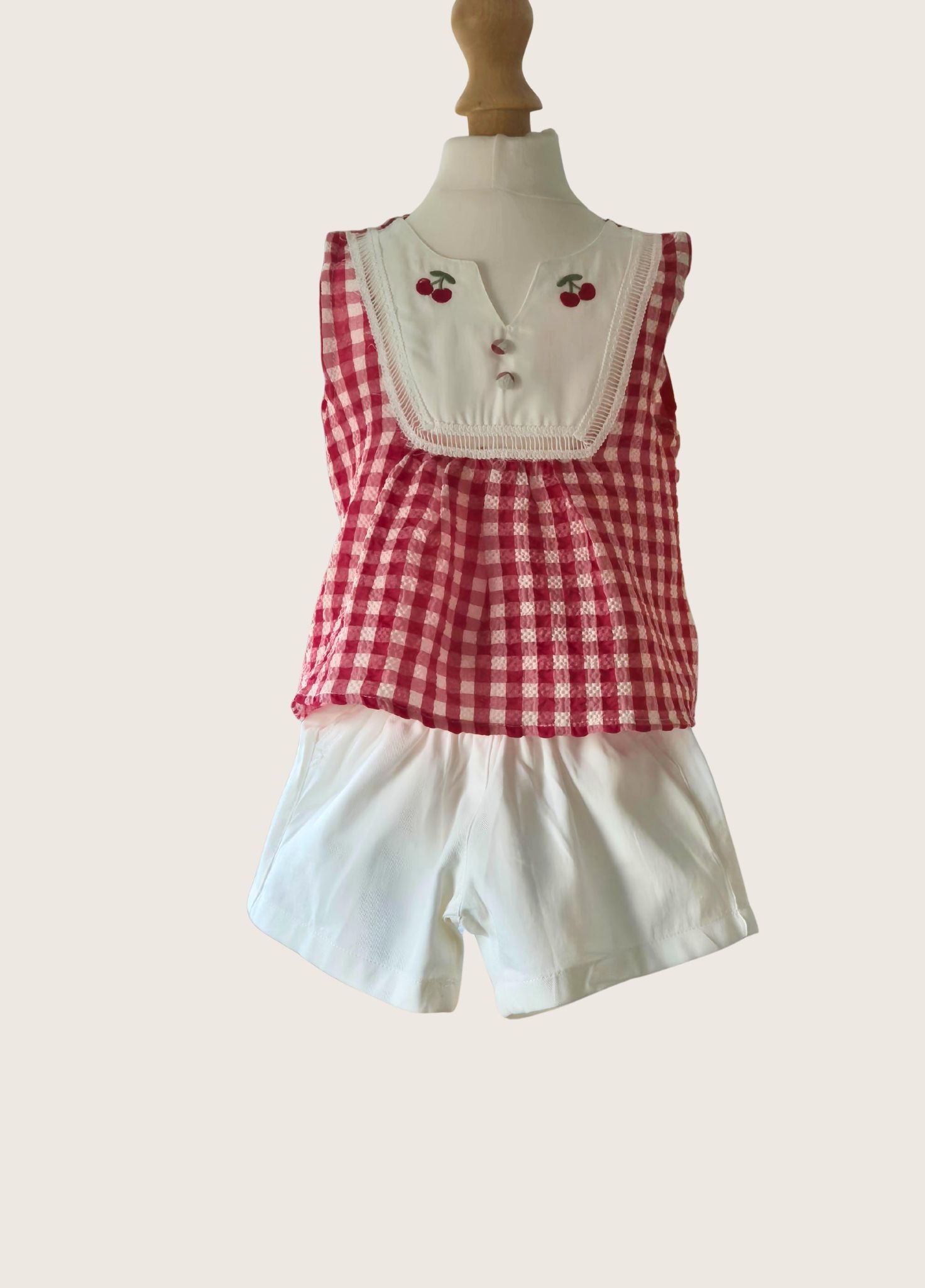 Red and white checkered top with white bibbed neckline and shorts on a mannequin against a white background